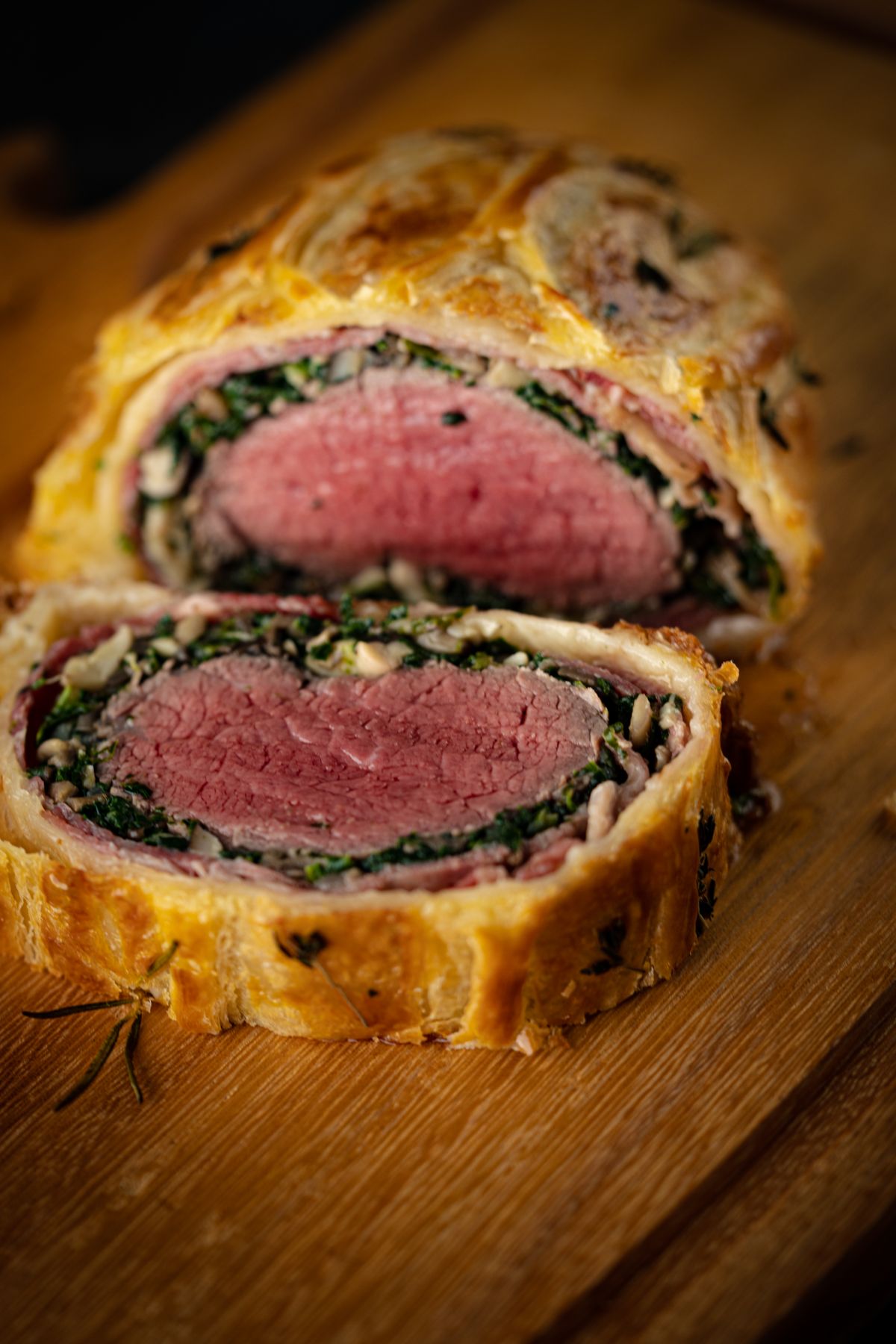 Two thick slices of beef wellington showing pink tenderloin, spinach layer and golden puff pastry