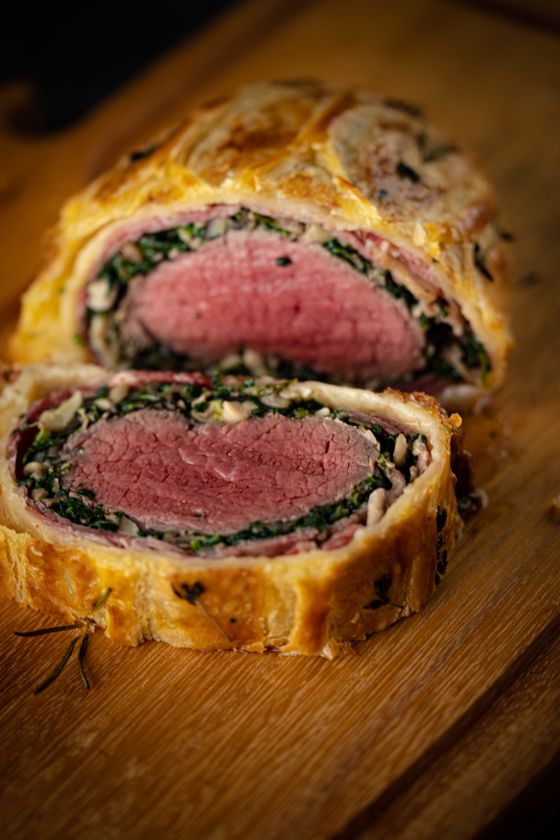 Two thick slices of beef wellington showing pink tenderloin, spinach layer and golden puff pastry