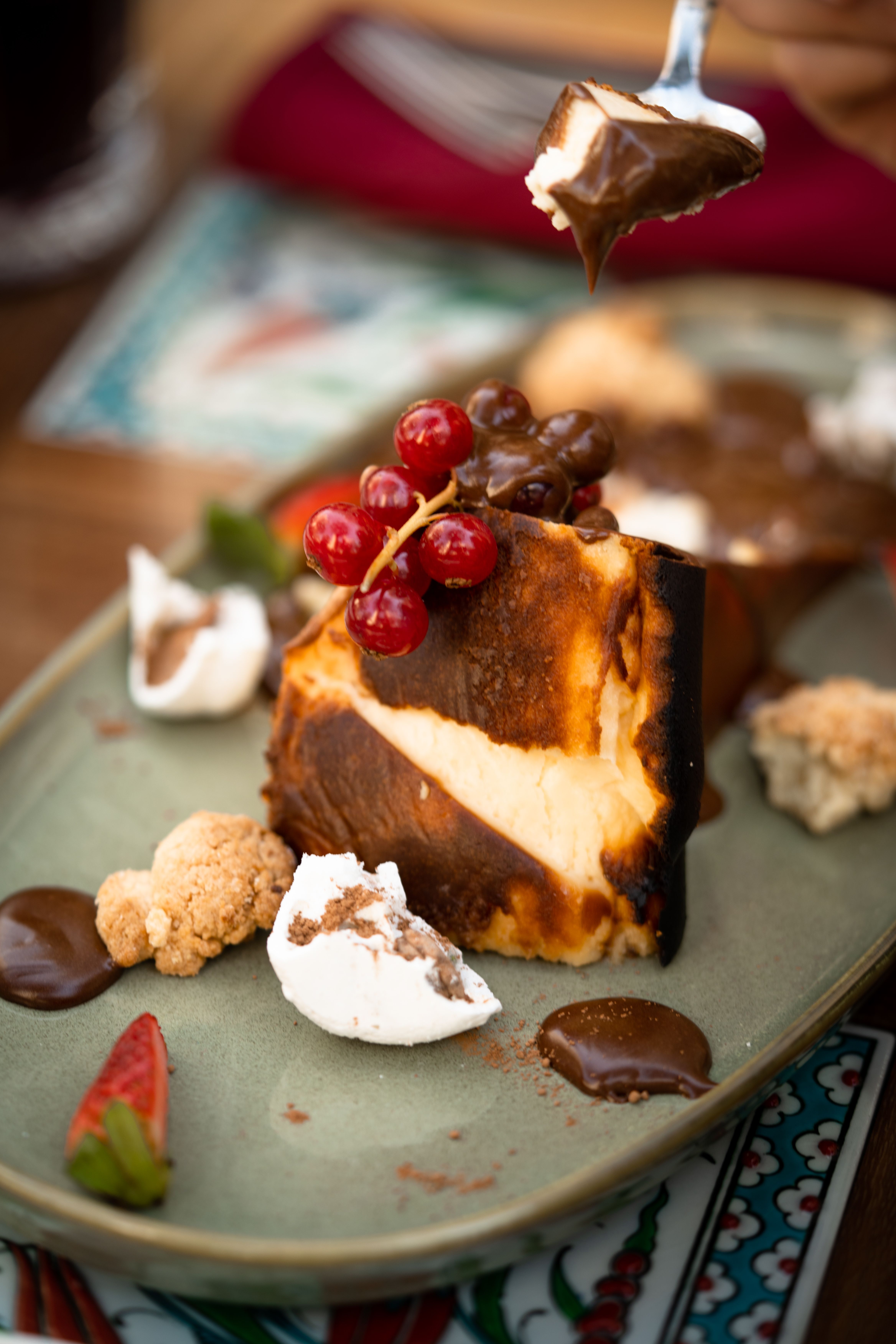 Rich Basque cheesecake topped with red currants and chocolate drizzle, elegantly presented.