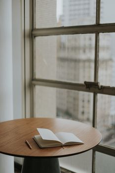 An inviting open notebook and pencil on a round table near a window, ideal for creative work.