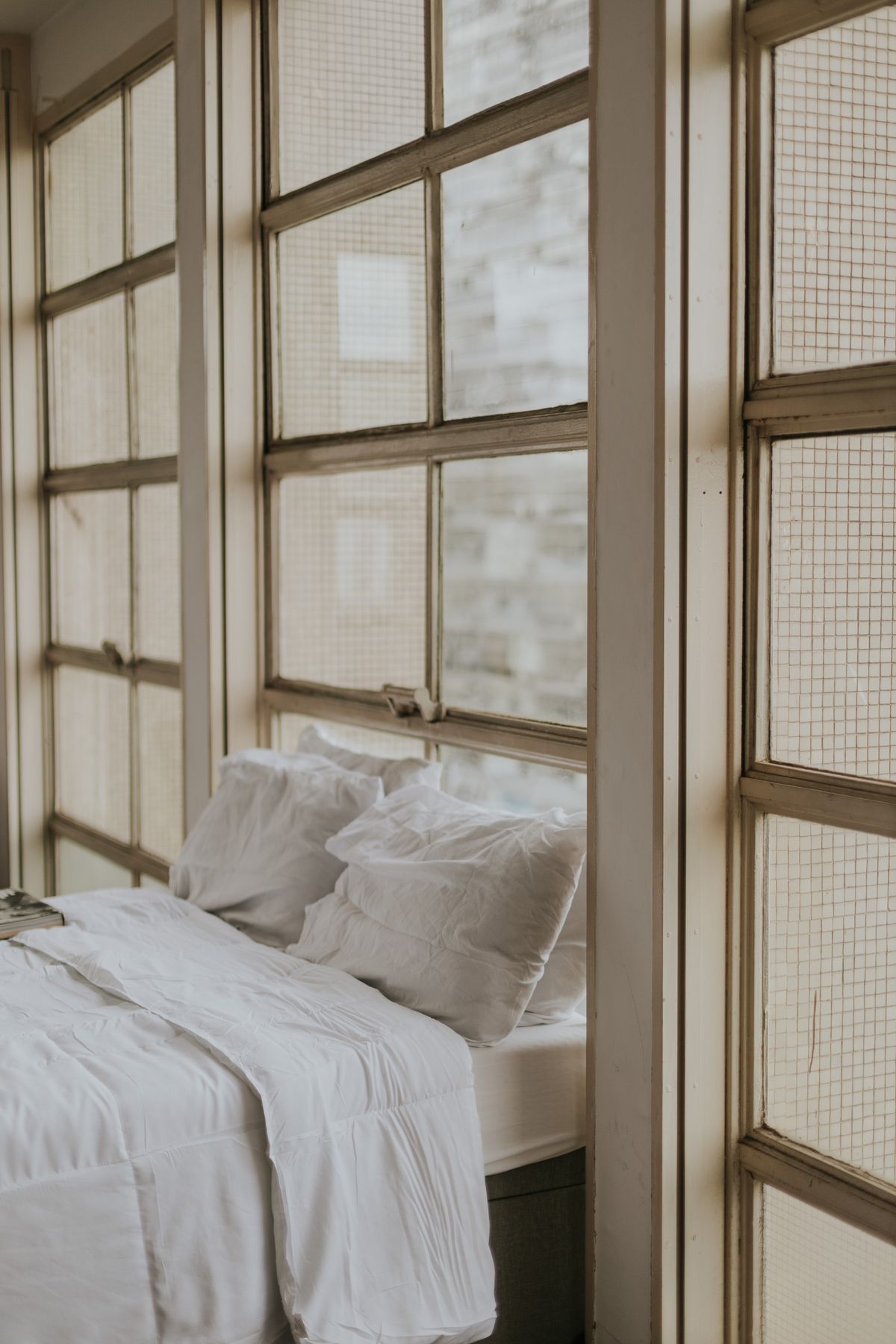 Stylish bedroom interior featuring a cozy bed and large vintage windows for natural light. Stock Photo.
