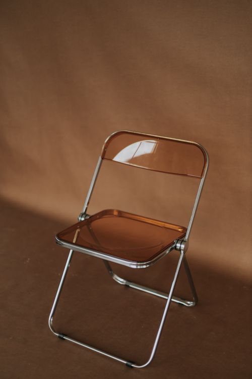 Free A sleek transparent folding chair sits against a neutral brown backdrop, perfect for minimalist design. Stock Photo