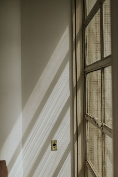 Free Soft sunlight casts geometric shadows on an interior wall beside a window. Stock Photo