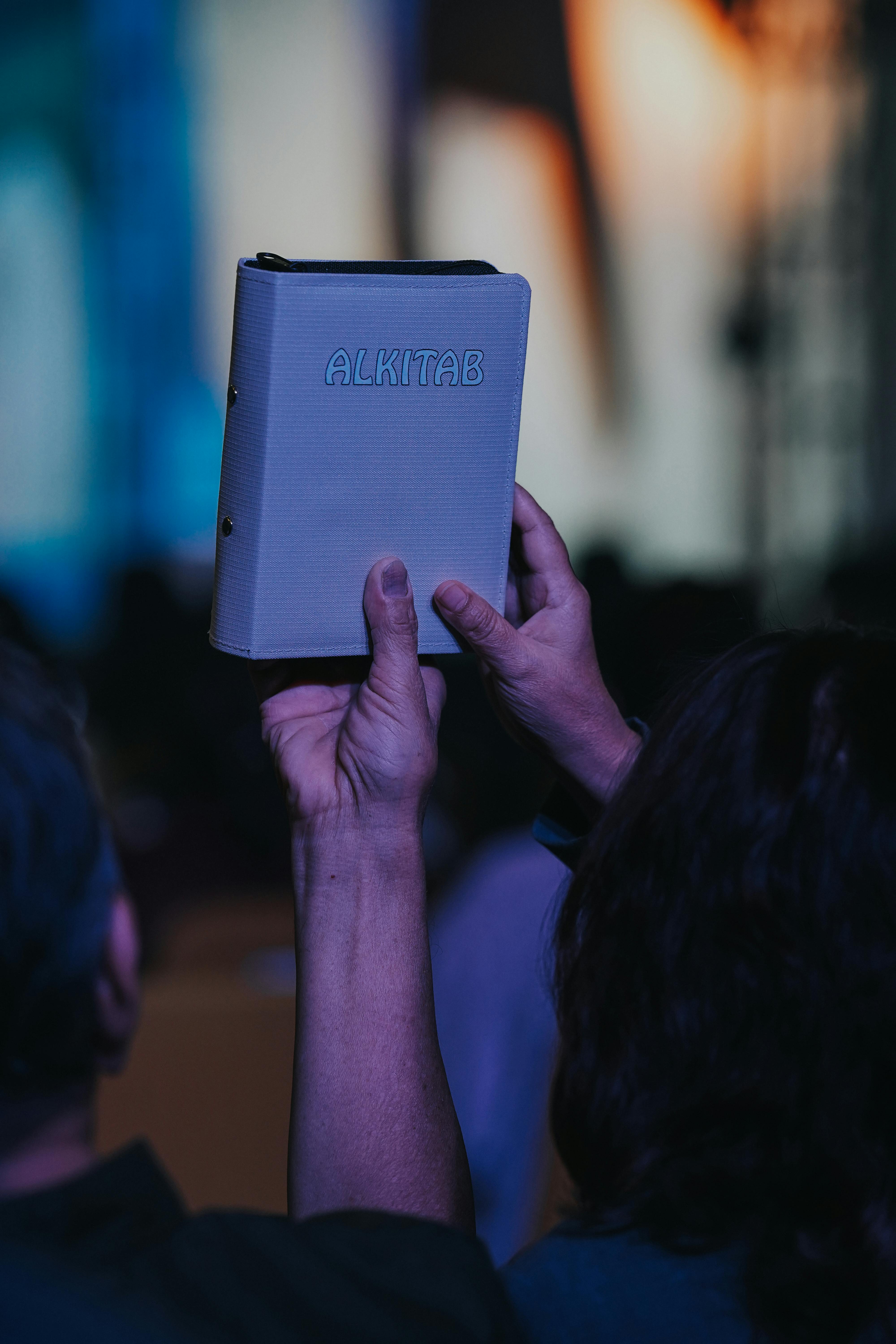 A person holds up an Alkitab Bible during a worship service, symbolizing faith and devotion.