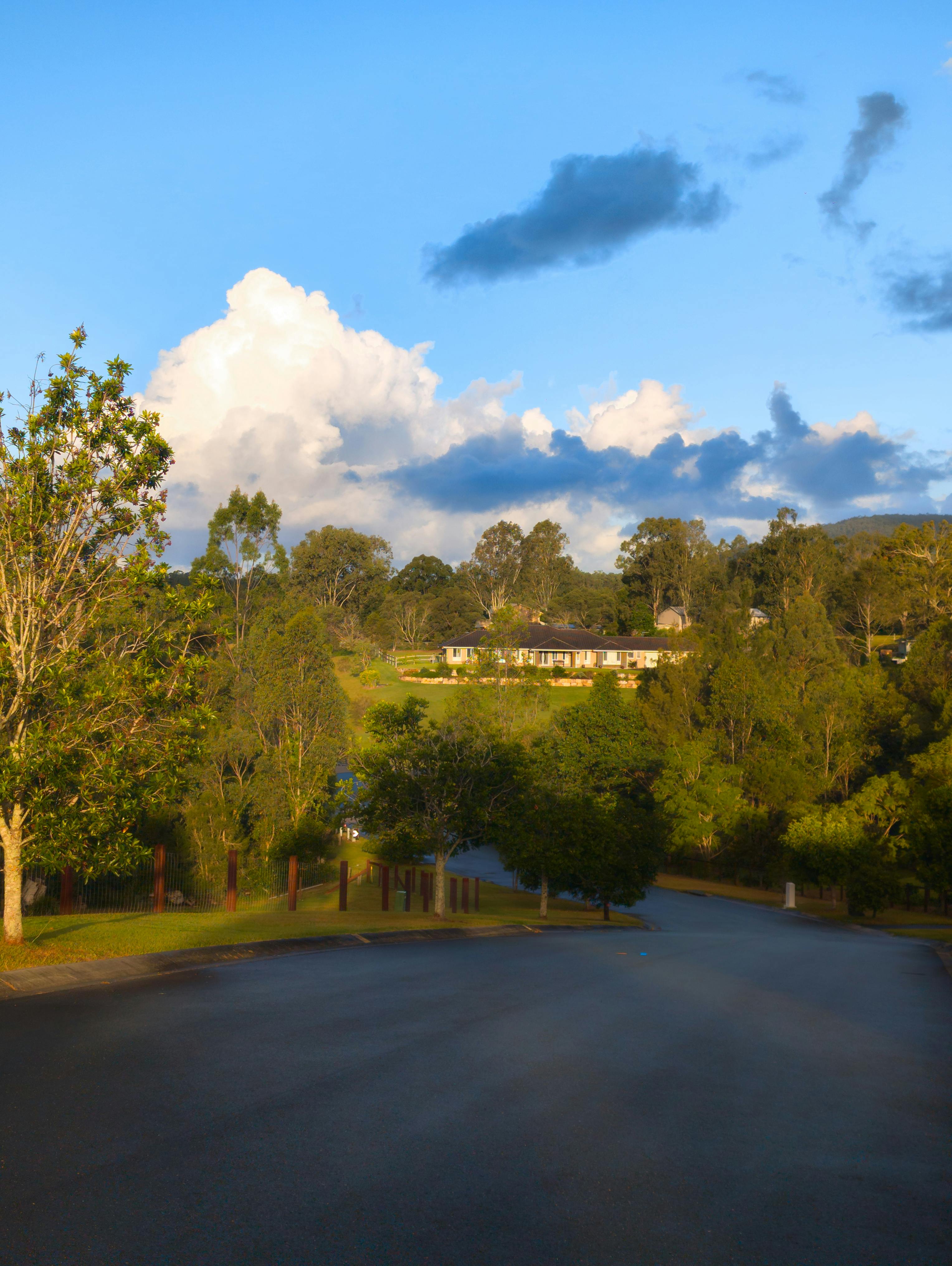 A picturesque rural scene with a house surrounded by trees under a vibrant blue sky with fluffy clouds.