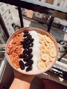 Delicious smoothie bowl with granola, blackberries, coconut, and bananas enjoyed on a sunny balcony.