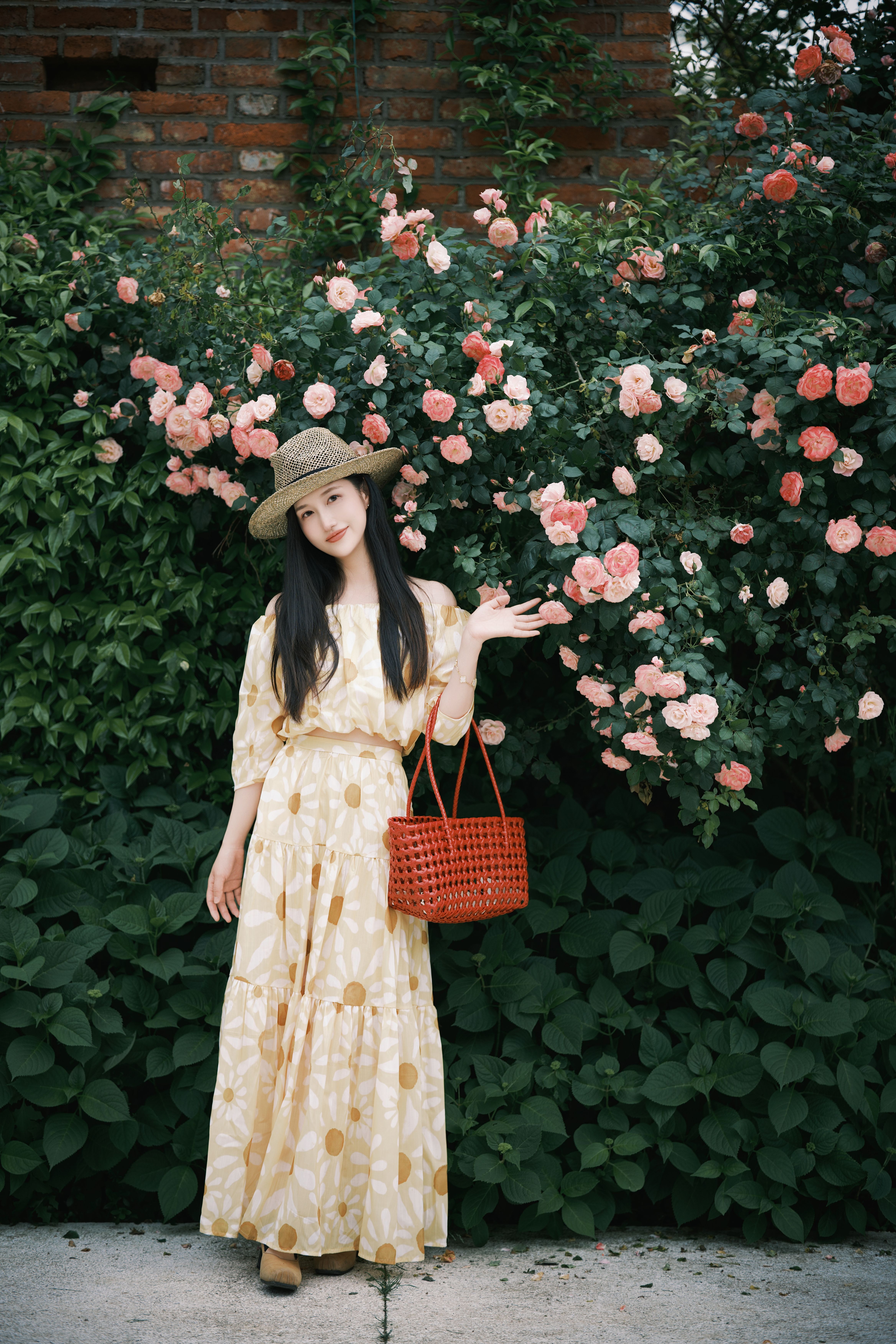 Elegant woman in a floral dress and hat beside blooming roses, perfect for summer vibes.