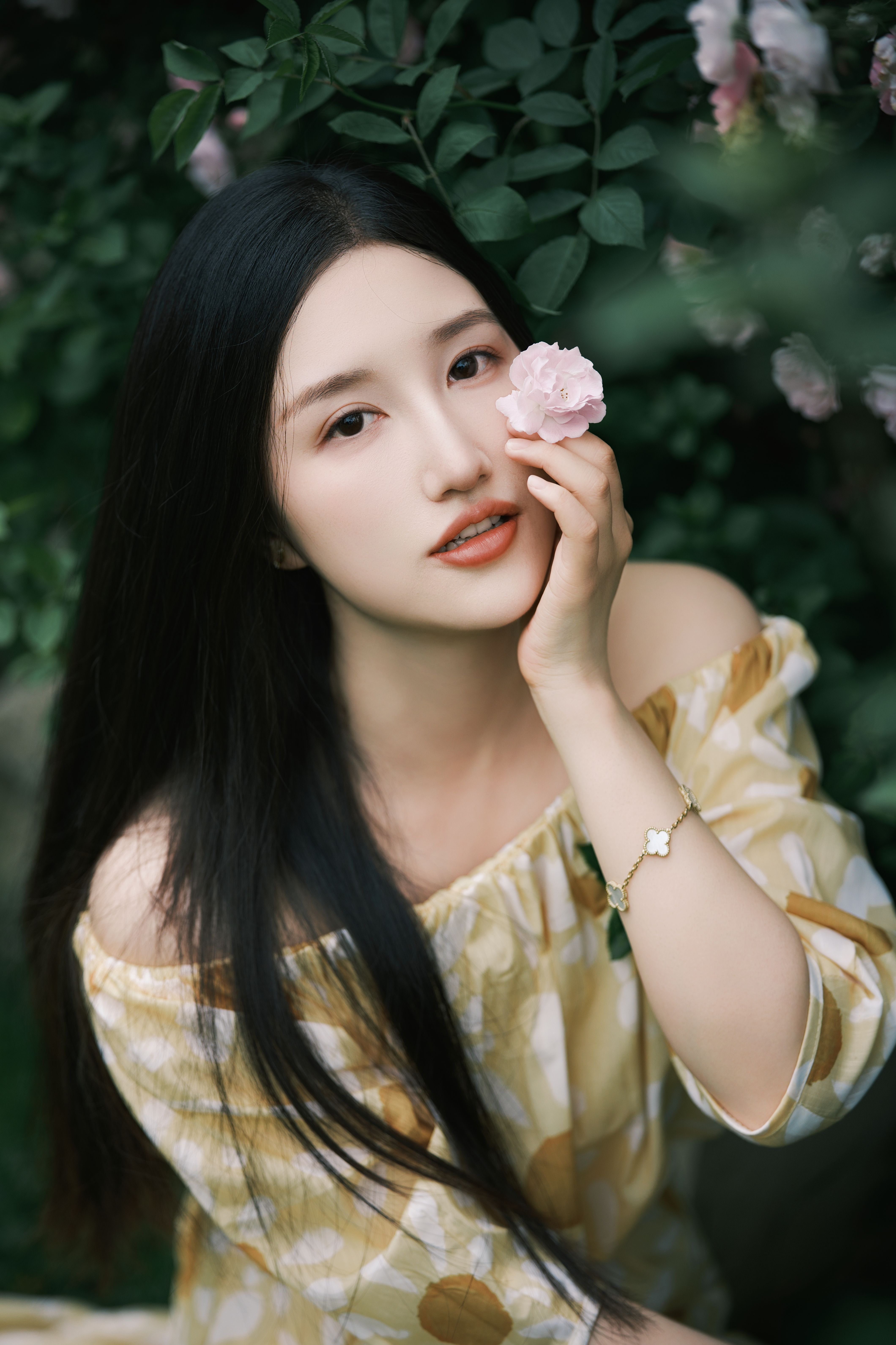 Elegant portrait of a woman touching a pink flower in a lush garden setting.