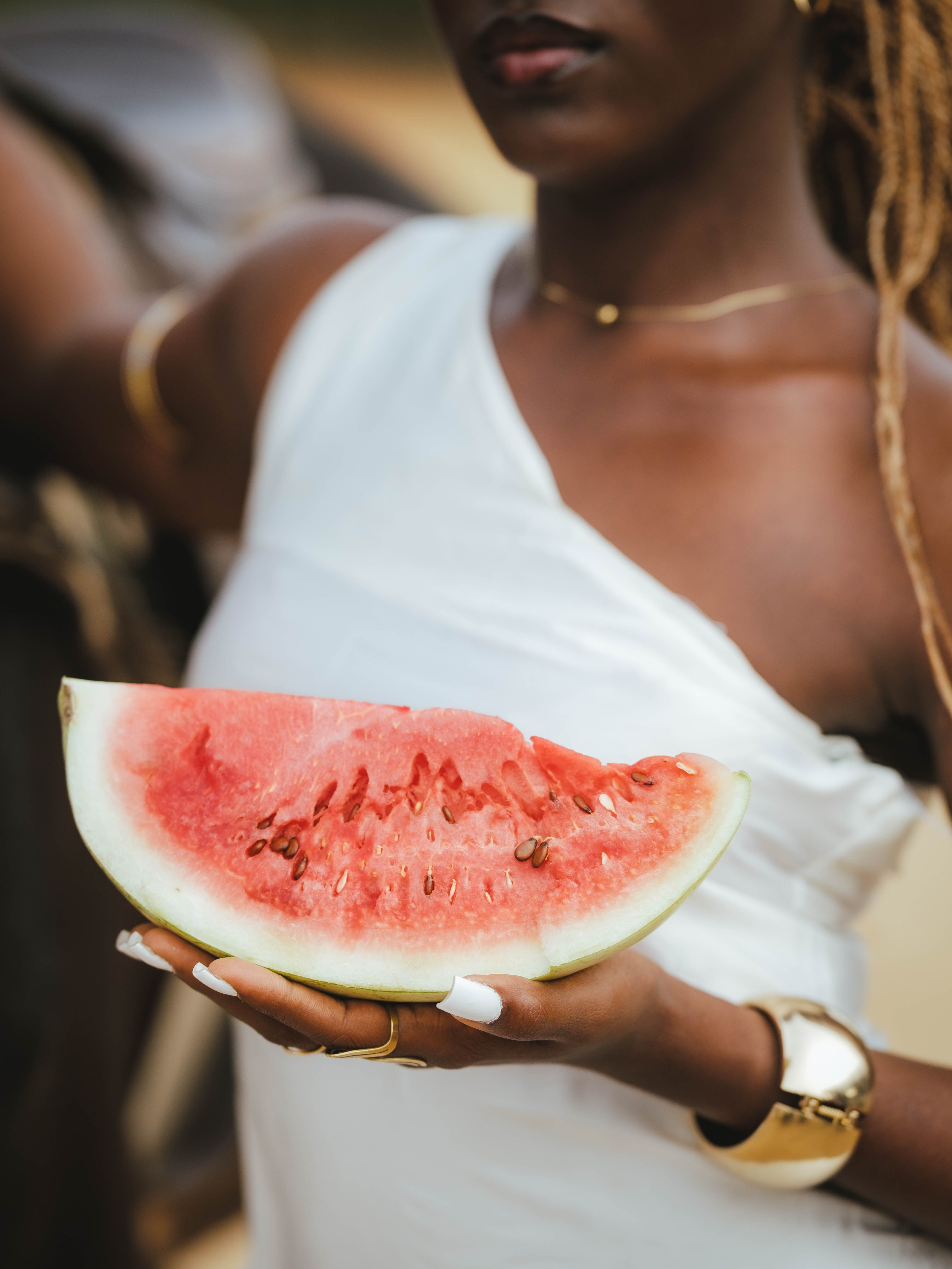 A woman in white holds a fresh slice of watermelon outdoors in Zaria, Nigeria.