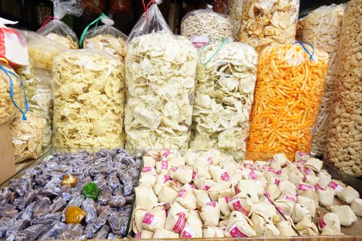 Assorted traditional snacks displayed in plastic bags and baskets at a local market, showcasing diverse textures and colors.