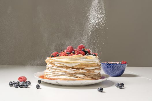 Delicious crêpe cake topped with fresh berries and dusted with sugar, perfect for dessert lovers.