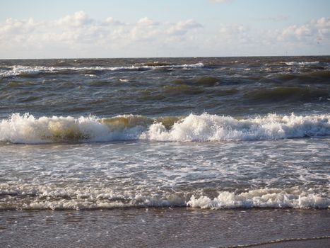 Capture the power of nature with ocean waves crashing on a sandy beach under a bright sky.