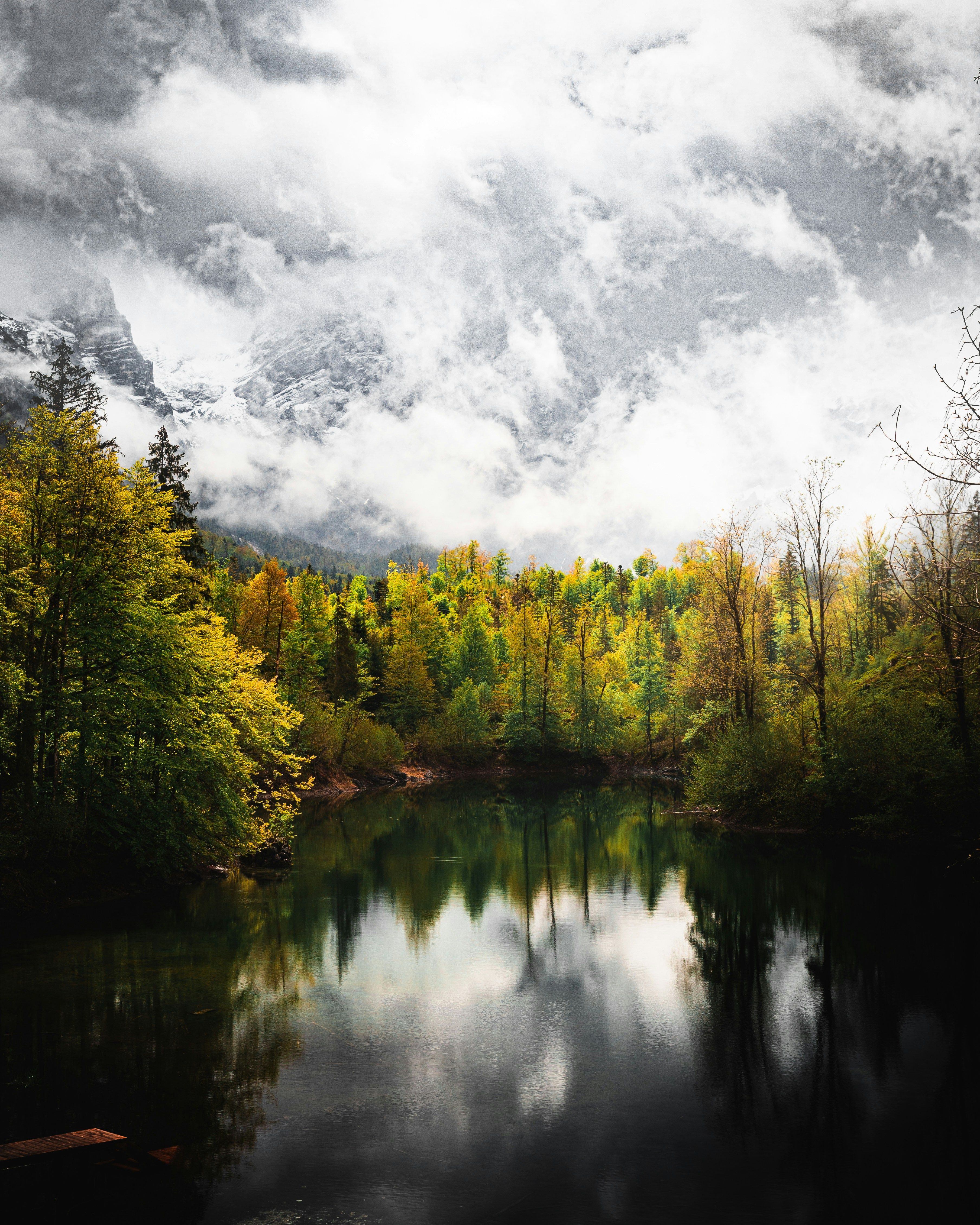 A tranquil lake surrounded by vibrant autumn forest under dramatic cloudy skies in Upper Austria.