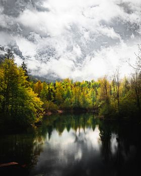 A tranquil lake surrounded by vibrant autumn forest under dramatic cloudy skies in Upper Austria.