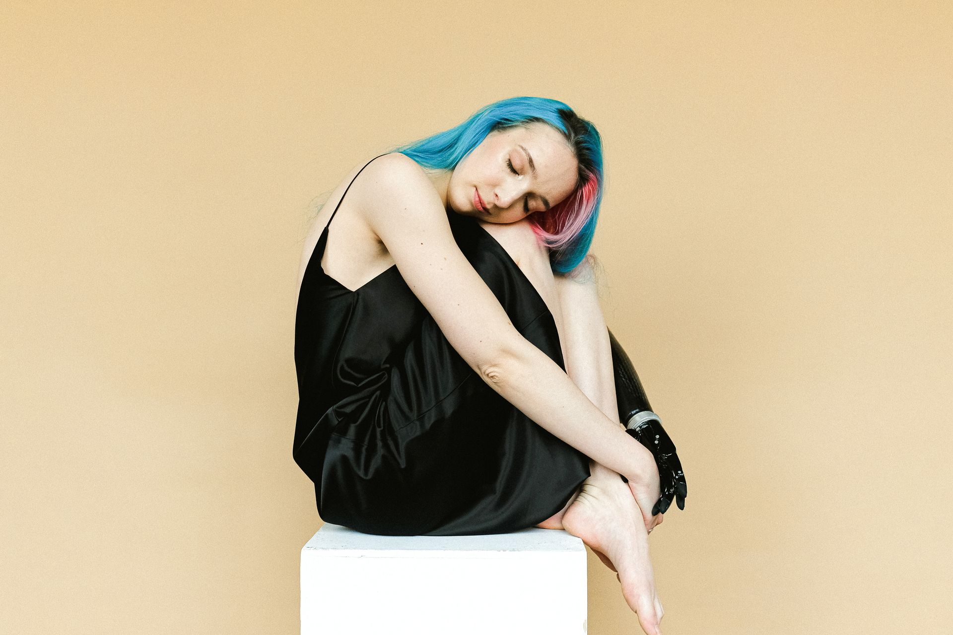 Colorful haired woman with a prosthetic arm sitting gracefully indoors, eyes closed.