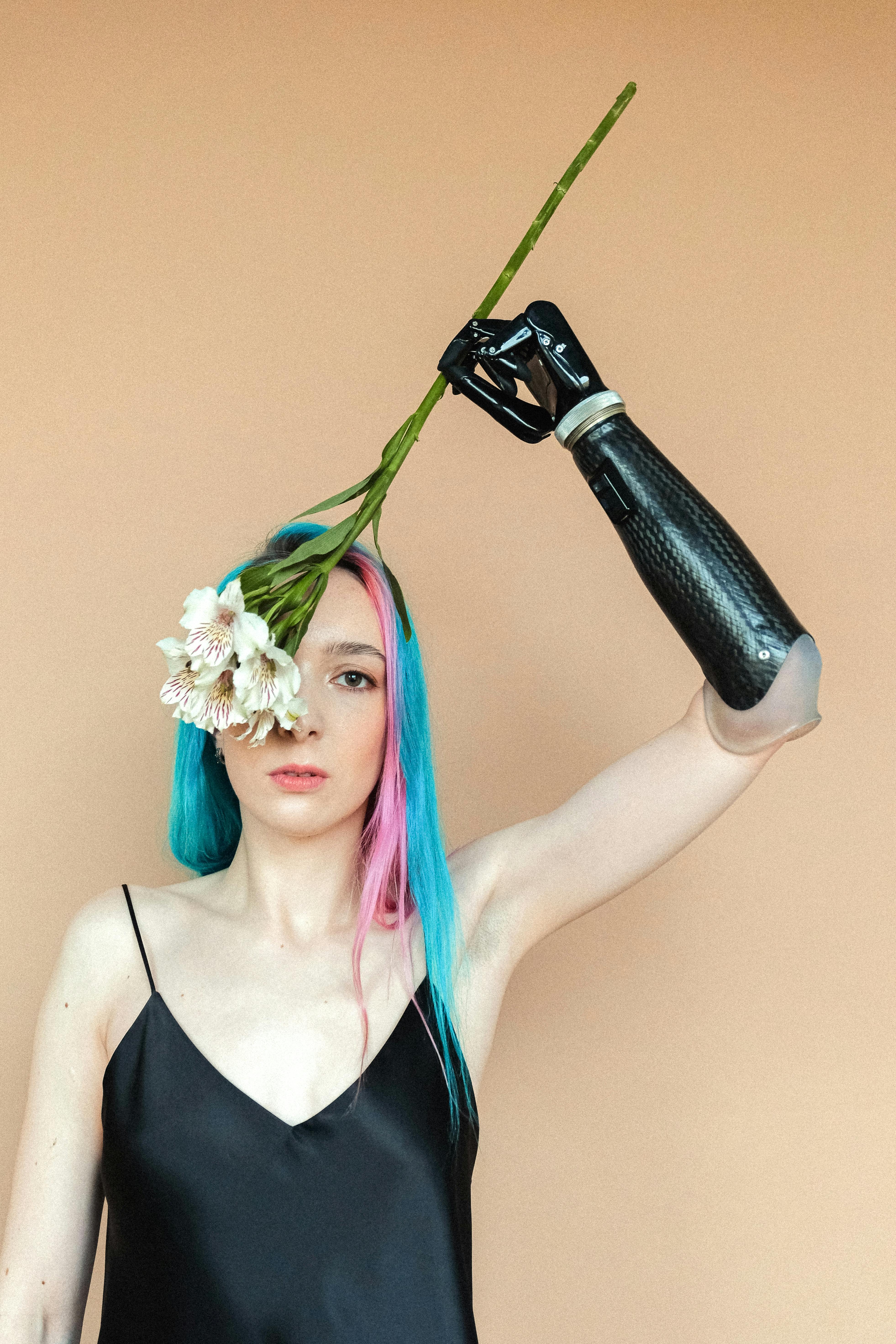 Woman with colored hair and prosthetic arm holding flowers, embracing diversity.