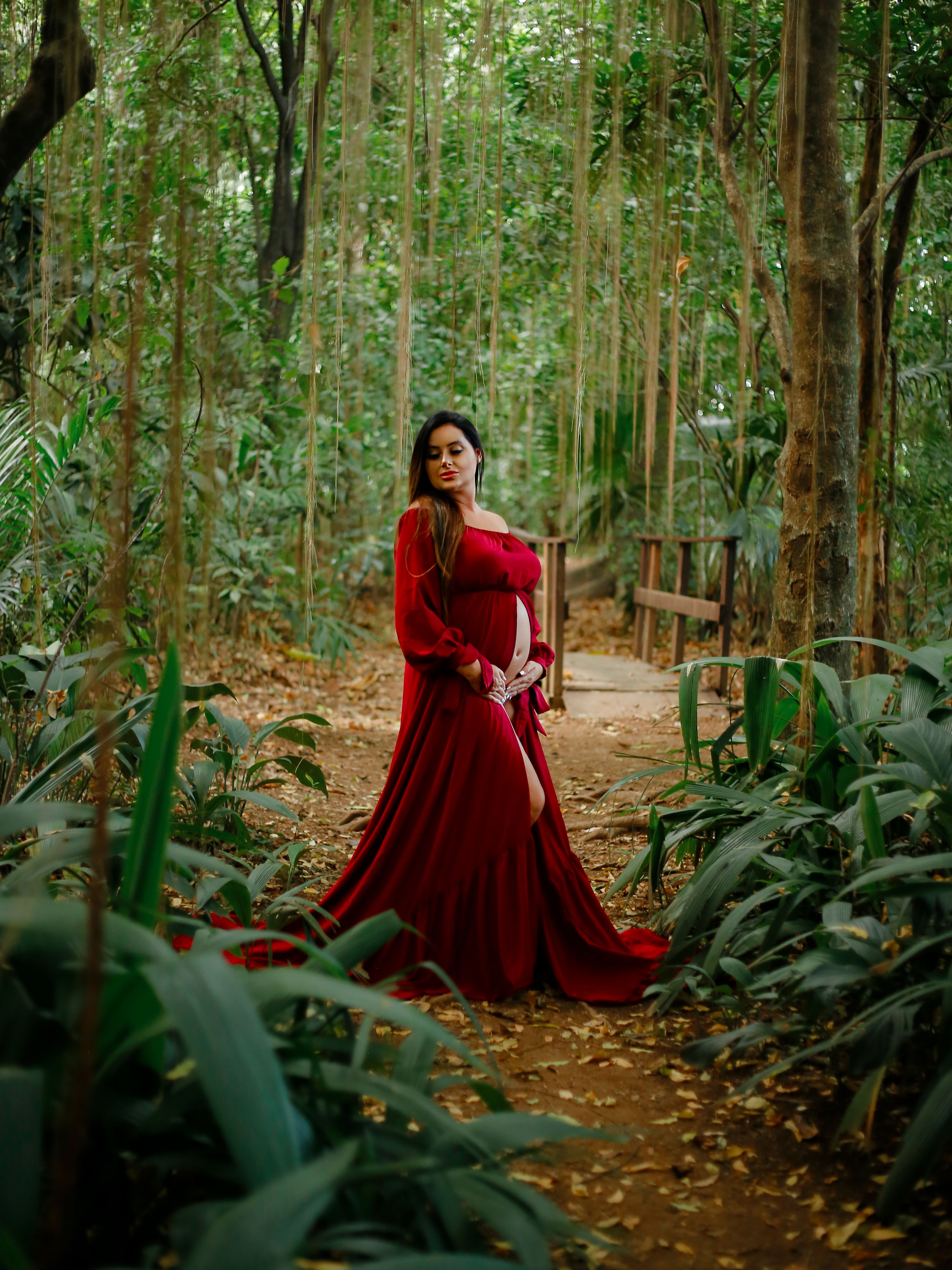 Pregnant Woman in Red Dress Posing in Lush Forest · Free Stock Photo