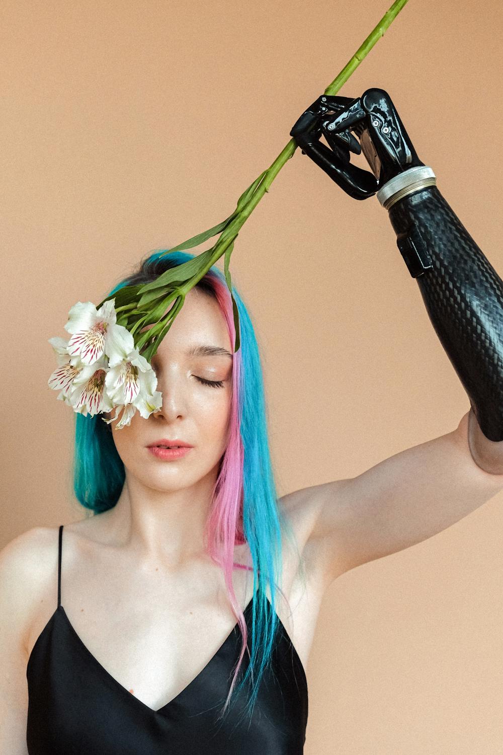 A woman with pink and blue hair holding flowers with a prosthetic arm.
