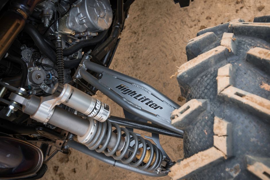 Detailed view of an ATV suspension and tire on sandy ground, emphasizing mechanical intricacies.