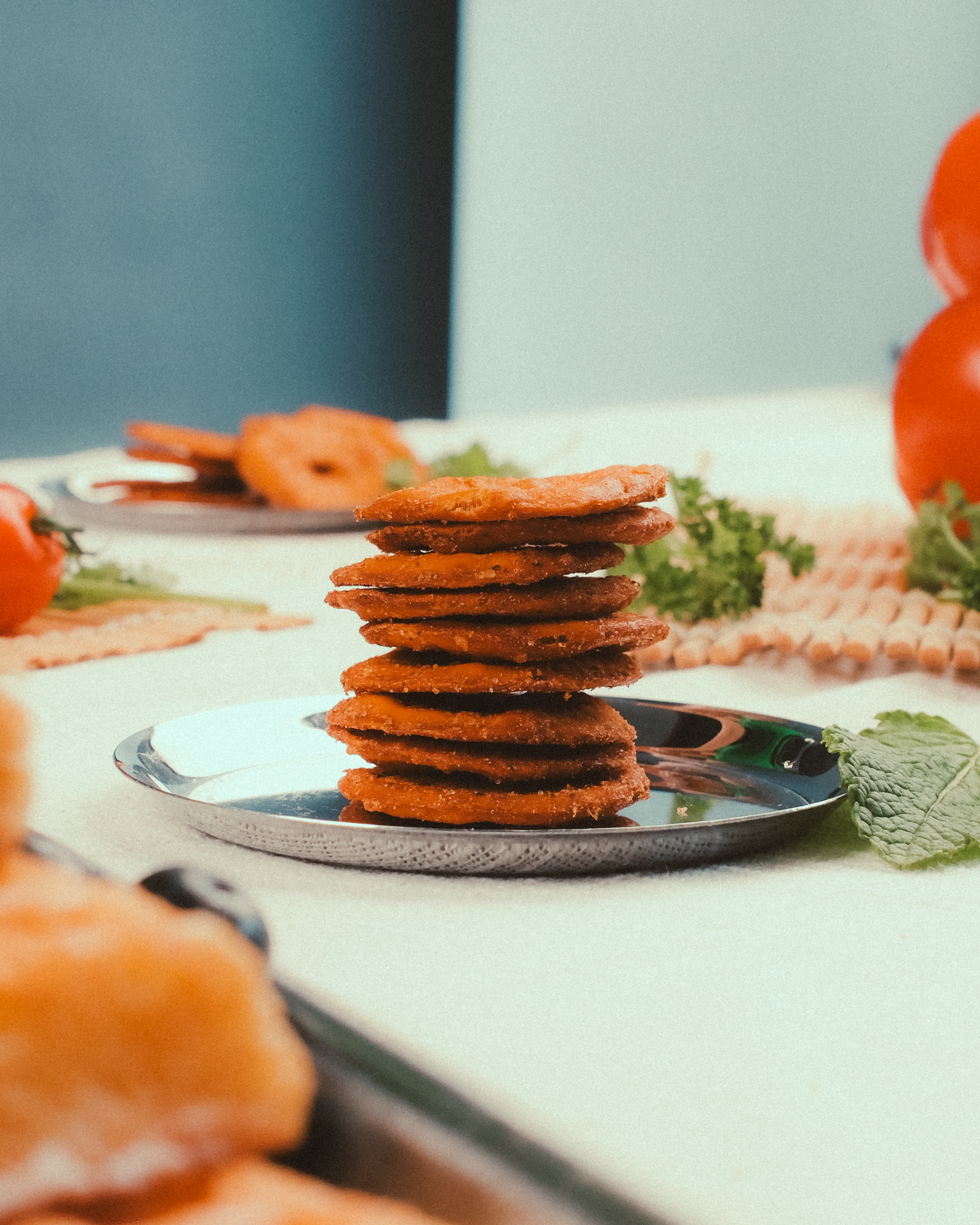 Close-up of stacked Indian snacks on a plate with tomatoes and mint leaves.