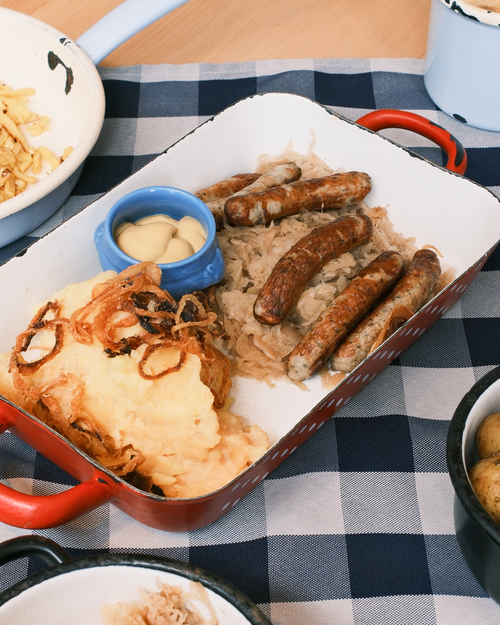 Free A hearty platter featuring German sausages, mashed potatoes, sauerkraut, and mustard on a checkered tablecloth. Stock Photo
