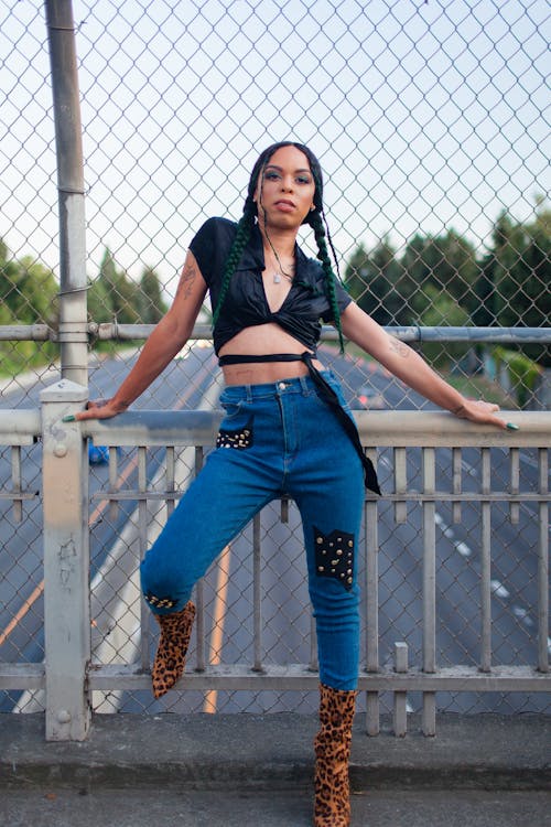 Vrouw In Zwarte Crop Top En Blauwe Denim Jeans Leunend Op Wit Metalen Hek
