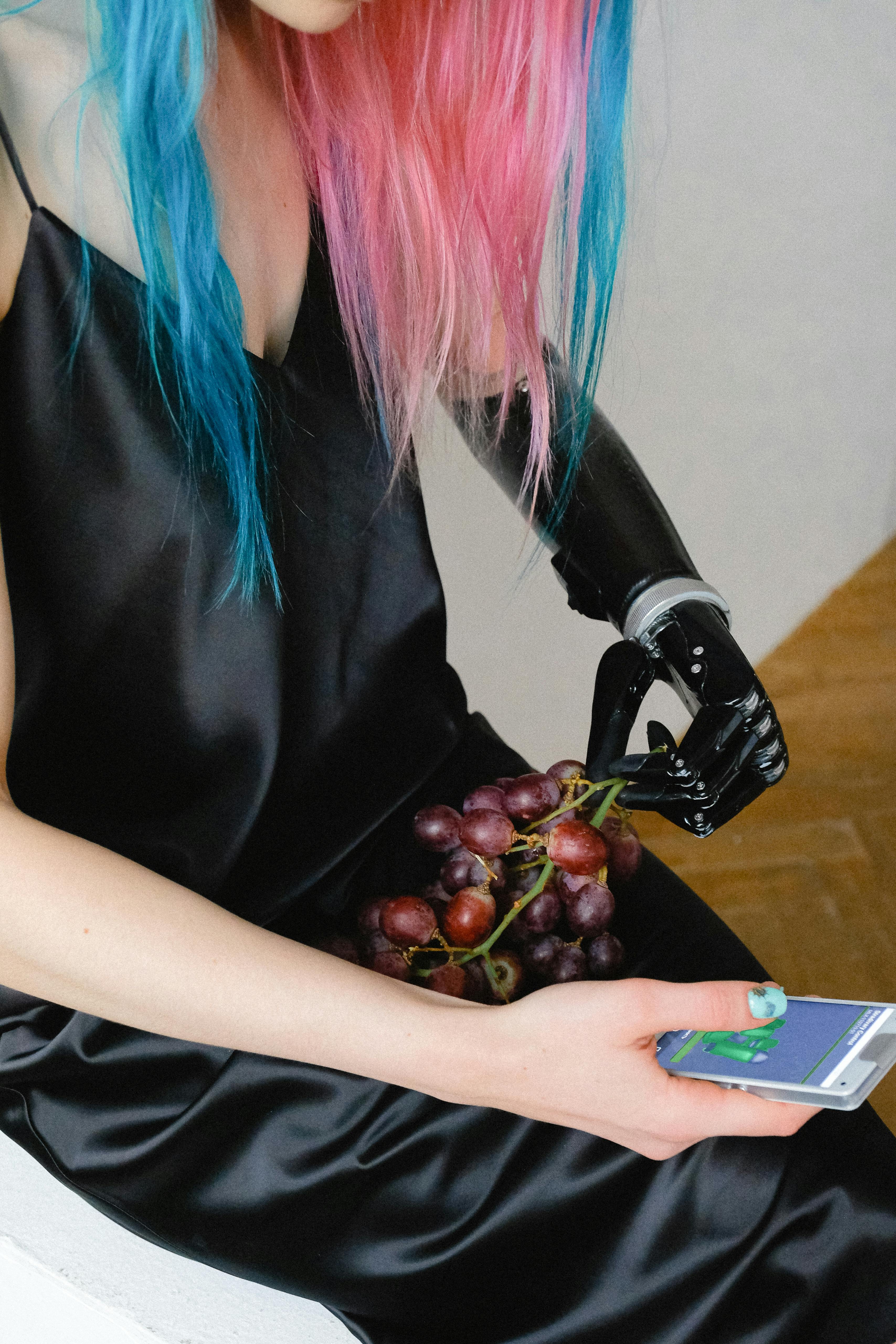 在室内环境中，一位现代女性用假肢手臂拿着葡萄和智能手机