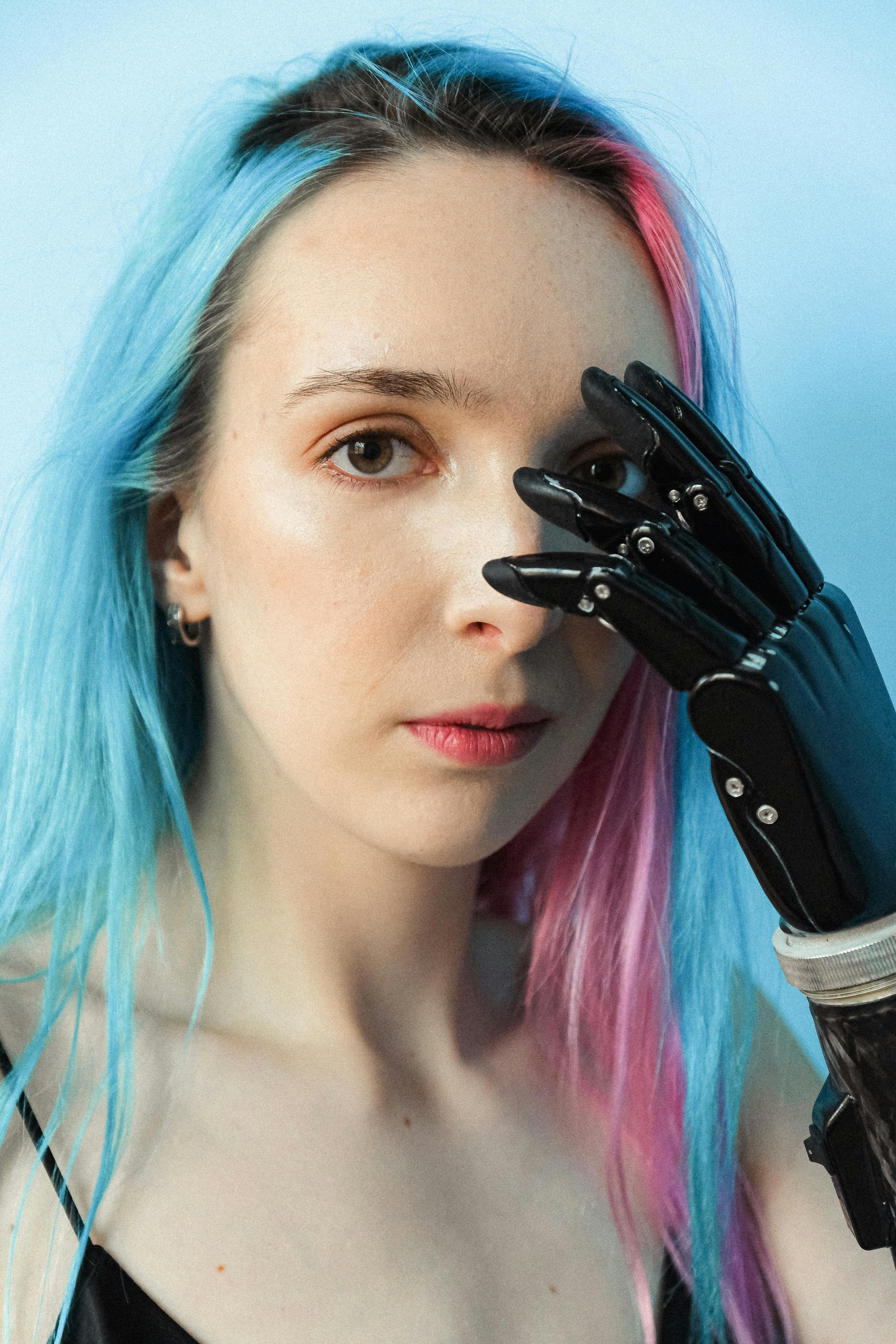 Adult woman with prosthetic arm and vibrant hair showcases uniqueness and strength against a pastel background.