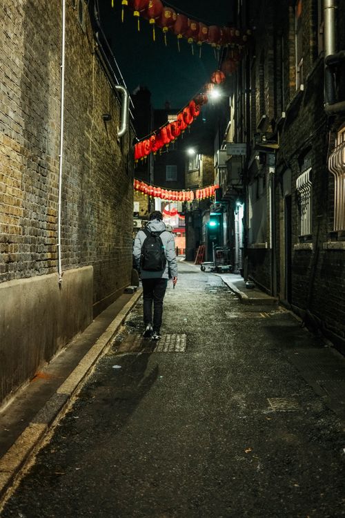 Free A person walks through a narrow alley in London, adorned with red lanterns at night. Stock Photo