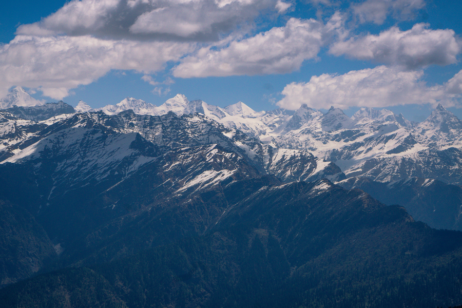 Stunning view of snow-capped mountains under a clear blue sky with fluffy clouds.