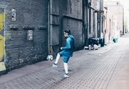 一名男子在城市小巷里练习足球，展现了城市体育文化