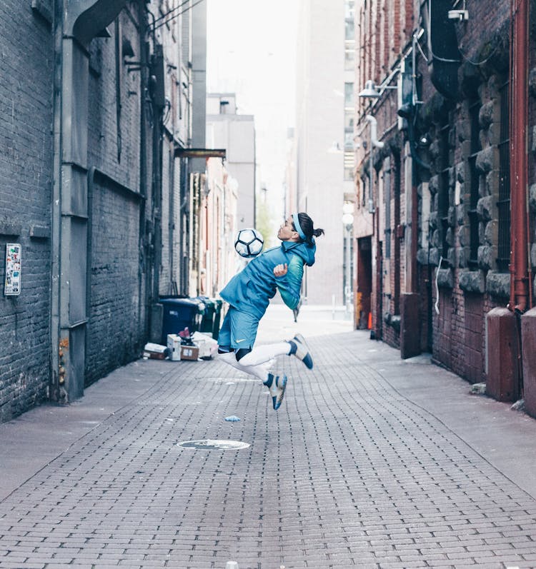 Male Football Player Jumping With Ball In City