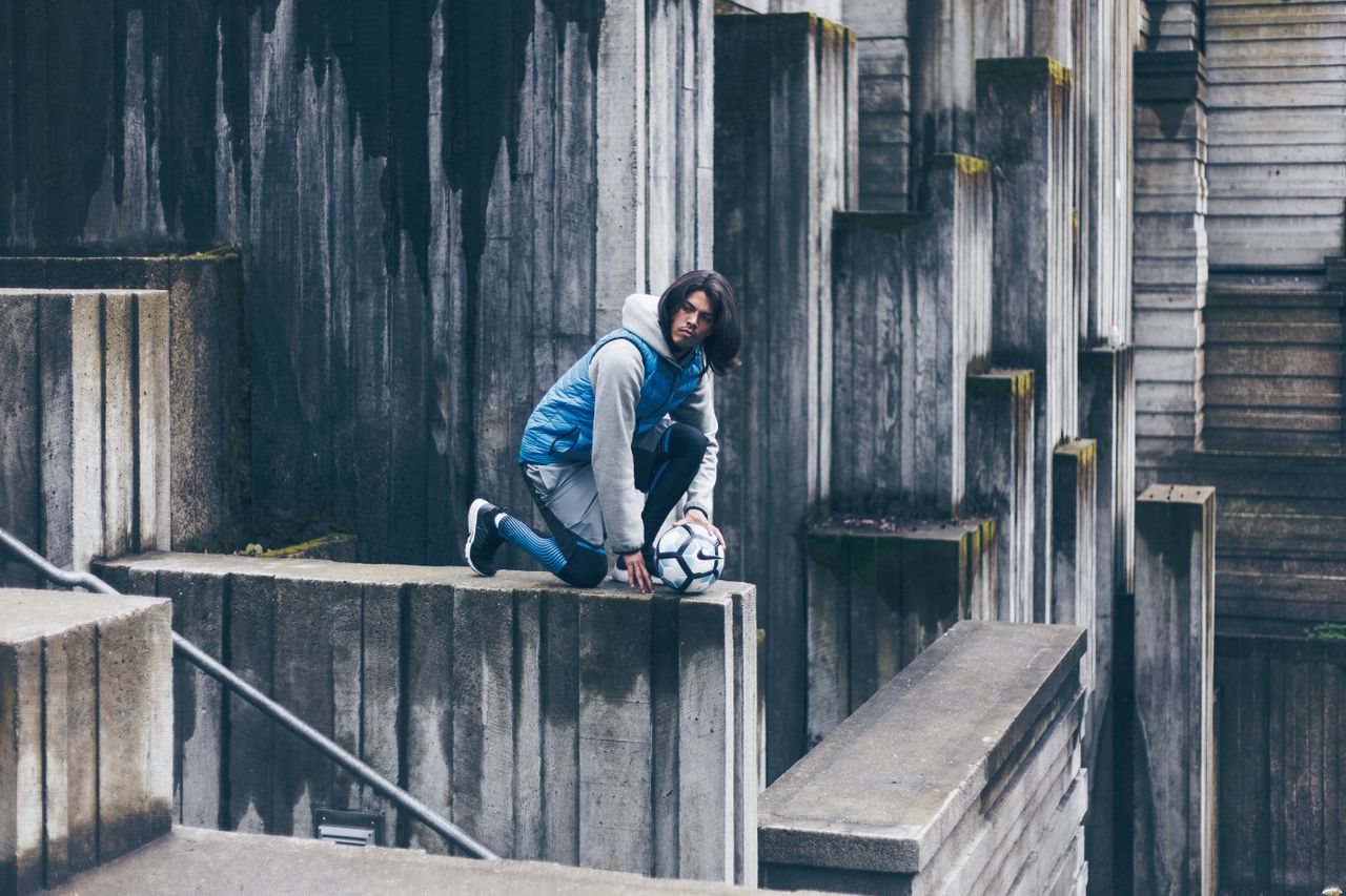 side view of concentrated male footballer sitting with ball on stone w