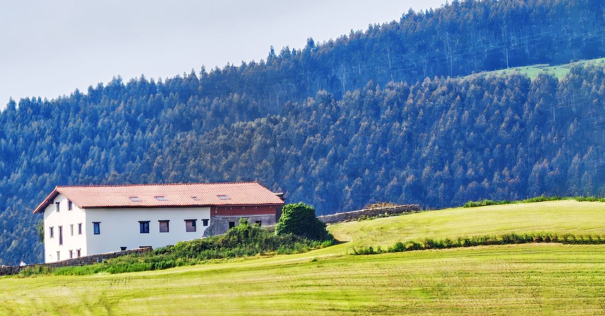 A charming white house nestled in lush greenery and hills, set against a forested backdrop.