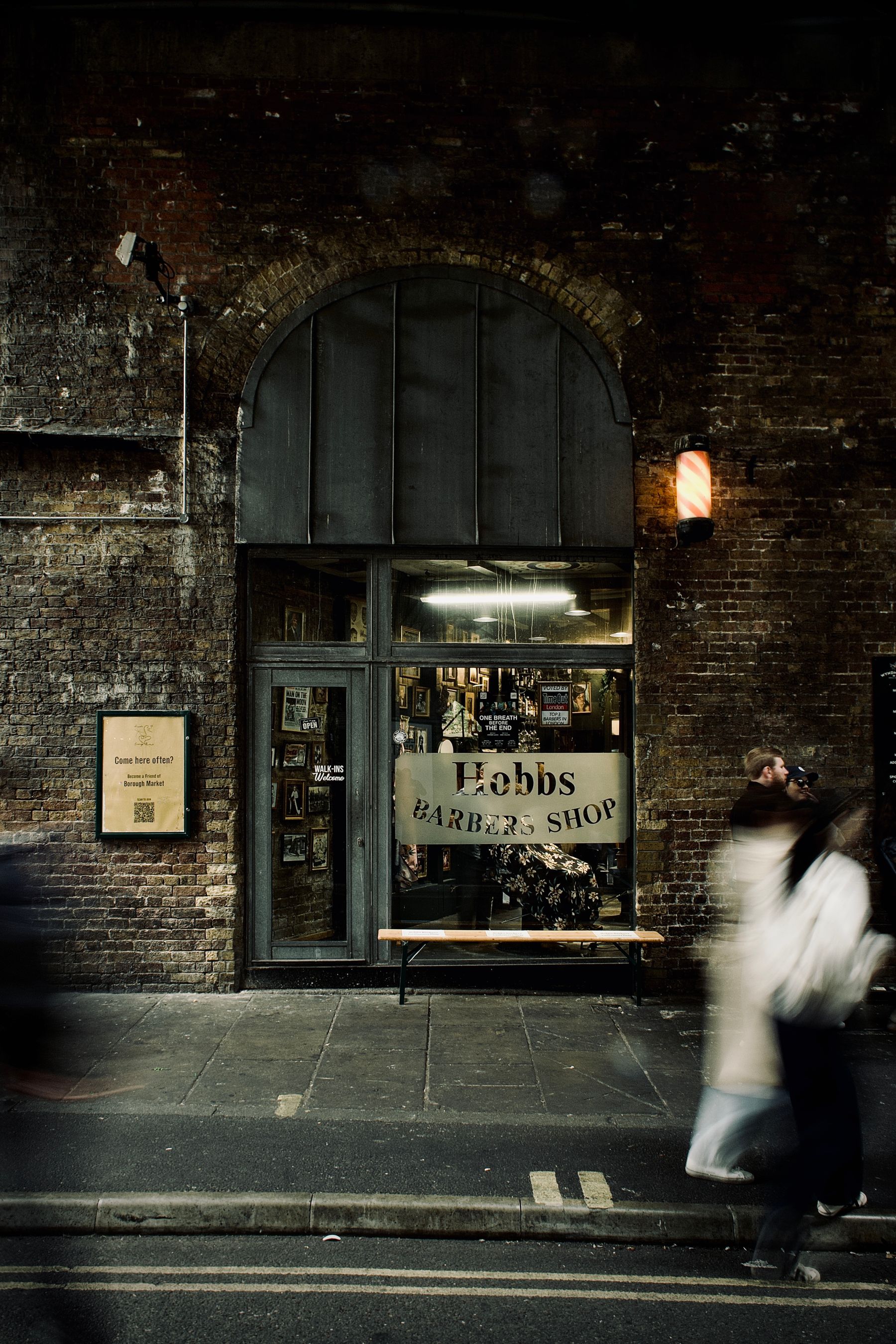 Vintage London barbershop with dark brickwork and a barber pole, photographed from the pavement