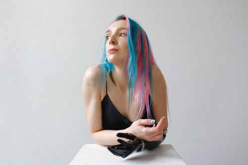 Free Artistic portrait of a woman with blue and pink hair and a prosthetic arm, looking thoughtful indoors. Stock Photo
