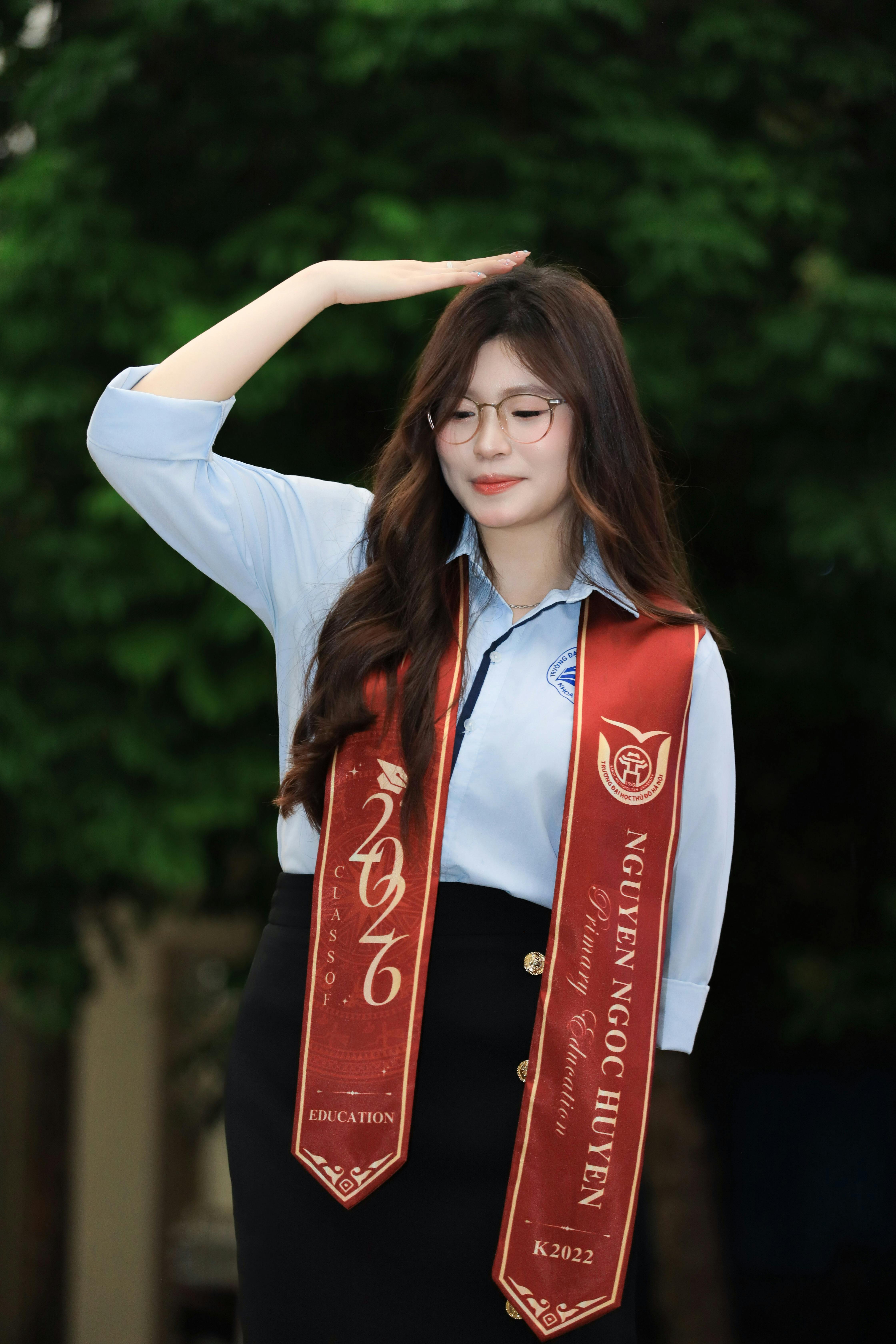 Smiling young woman celebrating graduation with red stole outdoors in Vietnam.