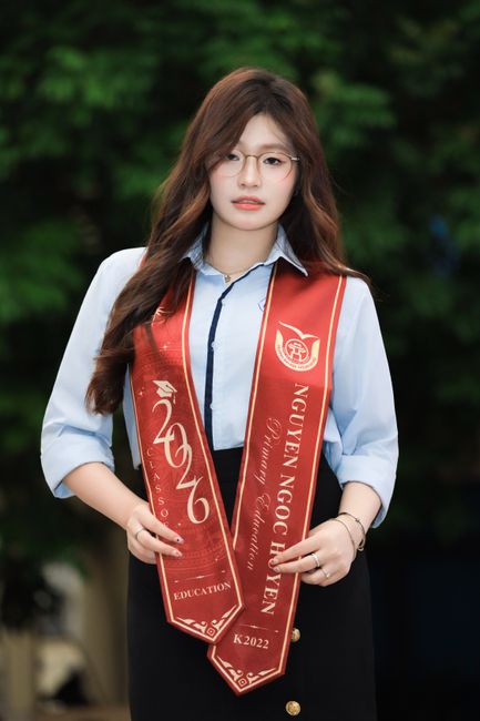 A young woman in graduation attire holds a sash outdoors, symbolizing academic achievement.