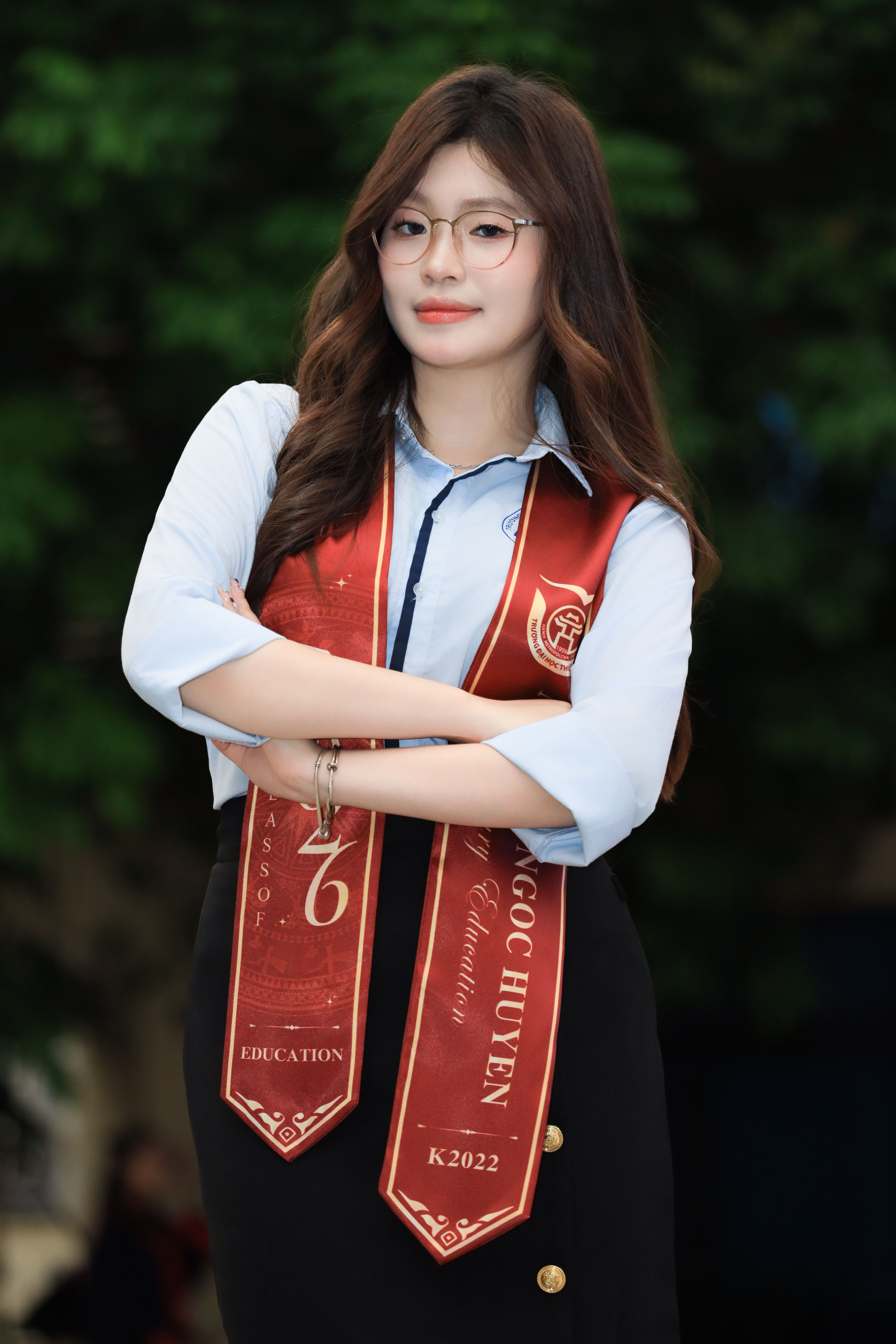 Young woman in graduation attire with sashes, smiling outdoors.