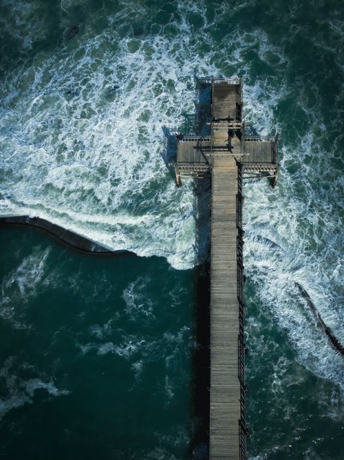 Free Stunning aerial shot of ocean waves crashing against a pier in Cape Town, South Africa. Stock Photo