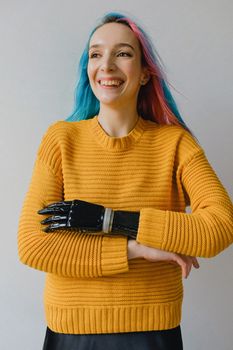 一位开朗的女人，留着粉蓝相间的头发，在室内穿着假肢和黄色毛衣