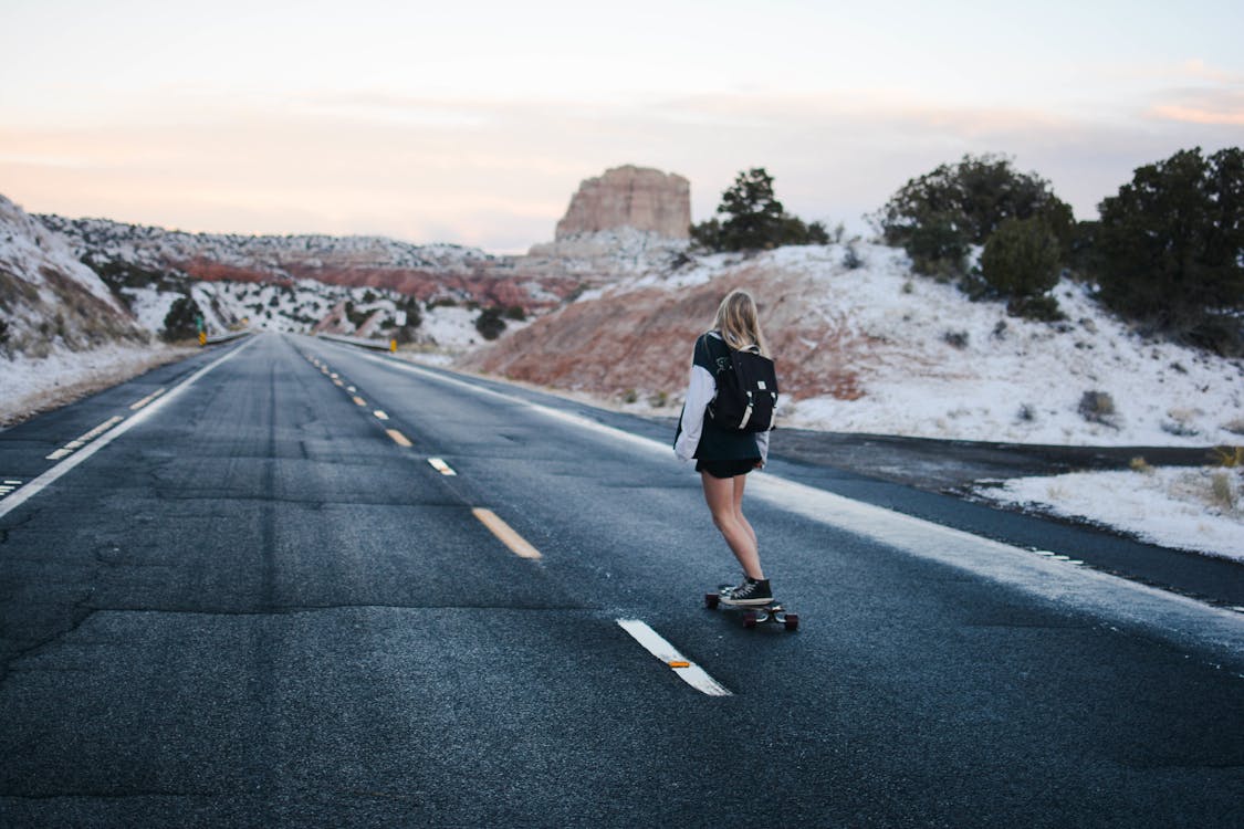 Free Woman in Black and White Long Sleeve Shirt Riding a Skateboard on a Freeway Road Stock Photo