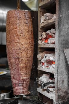 Close-up of a traditional Turkish döner kebab cooking on a rotisserie with glowing coals.