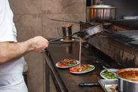 A chef prepares authentic Turkish kebabs, drizzling sauce over plated dishes in a Bursa kitchen.