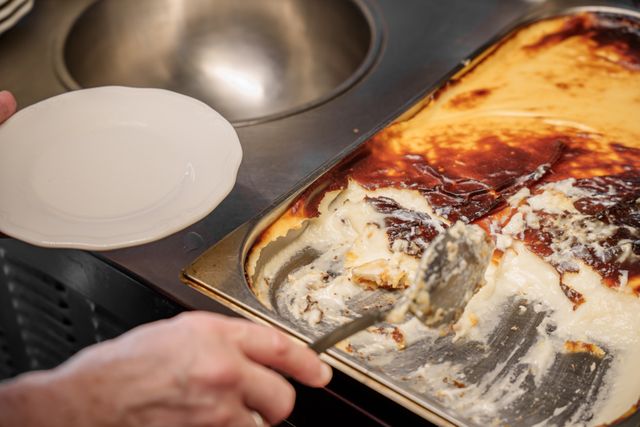 A person serving traditional Turkish rice pudding from a tray, showcasing its creamy texture.