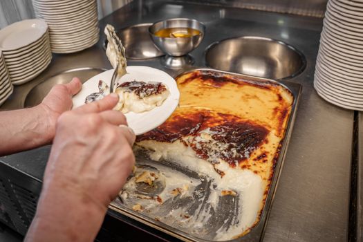 Close-up of hands serving Kazandibi, a traditional Turkish dessert, from a tray in a kitchen.