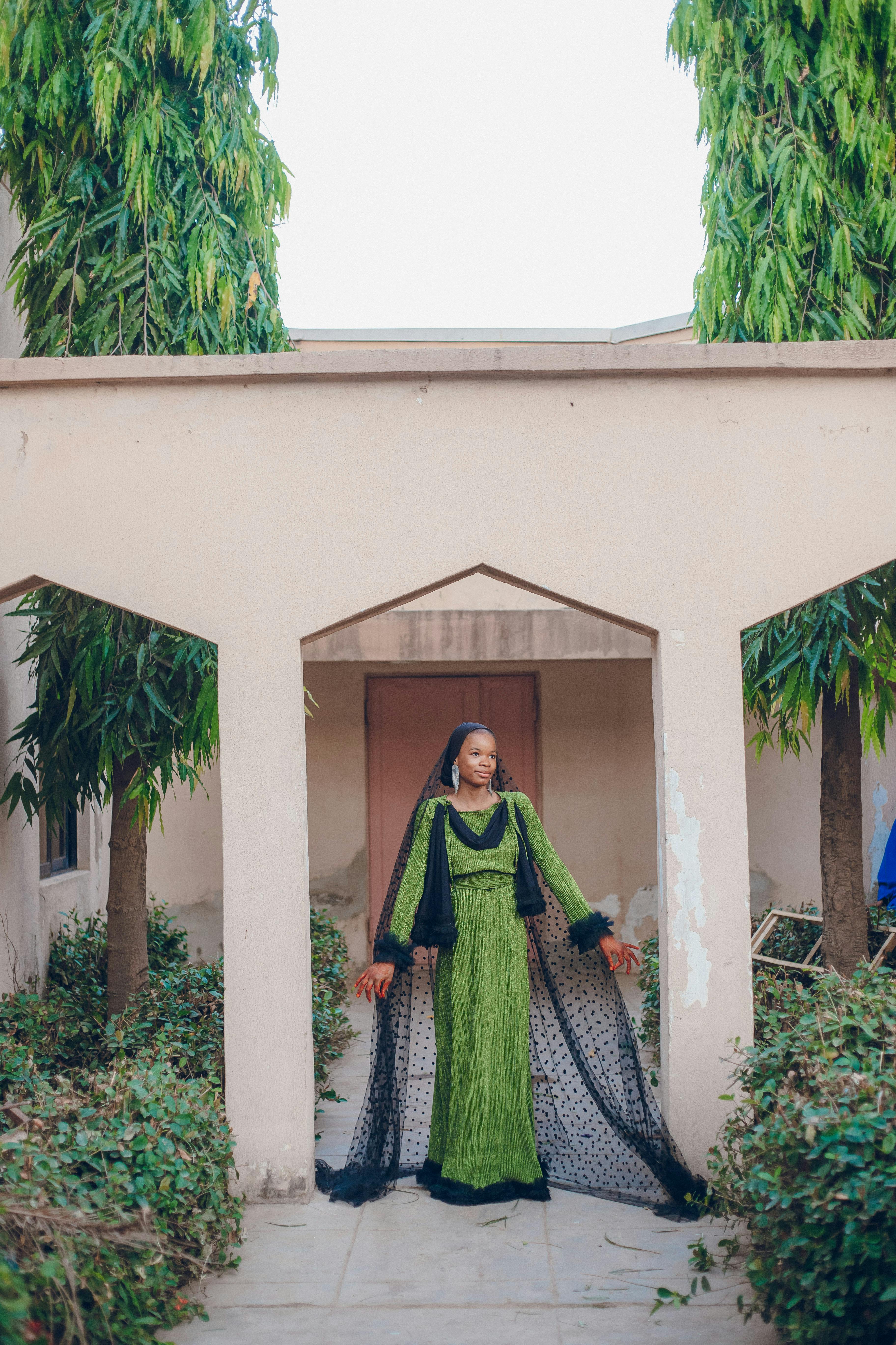 A graceful woman in a green dress poses elegantly under a decorative outdoor archway.
