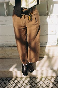 Fashionable outfit featuring cropped trousers, leather loafers, and herringbone belt in Lisbon's classic style.