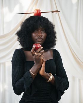 Stunning portrait of a woman in black attire holding an apple, with an apple pierced by an arrow on her head.