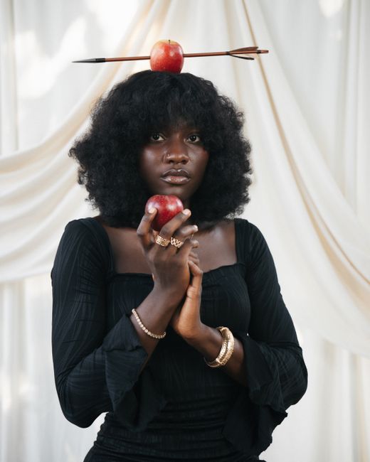 Stunning portrait of a woman in black attire holding an apple, with an apple pierced by an arrow on her head.